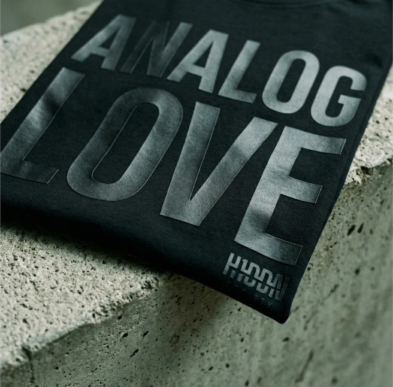 Close-up of satin-black Analog Love lettering on dense cotton, resting on concrete